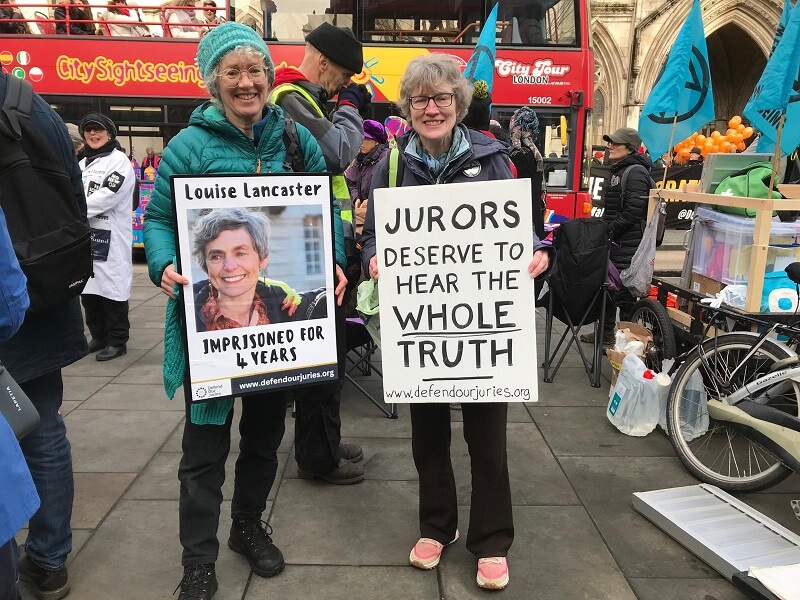 Two protestors hold placards. The first placard says: Lousie Lancaster Imprisoned for four years. The second placard says: Jurors deserve to hear the whole truth