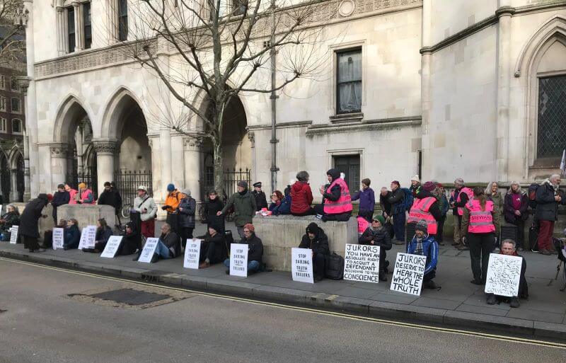 Protestors sit on pavement outside Royal Courts of Justice. They hold placards in support of Just Stop Oil activists sentenced to prison for peaceful protest.